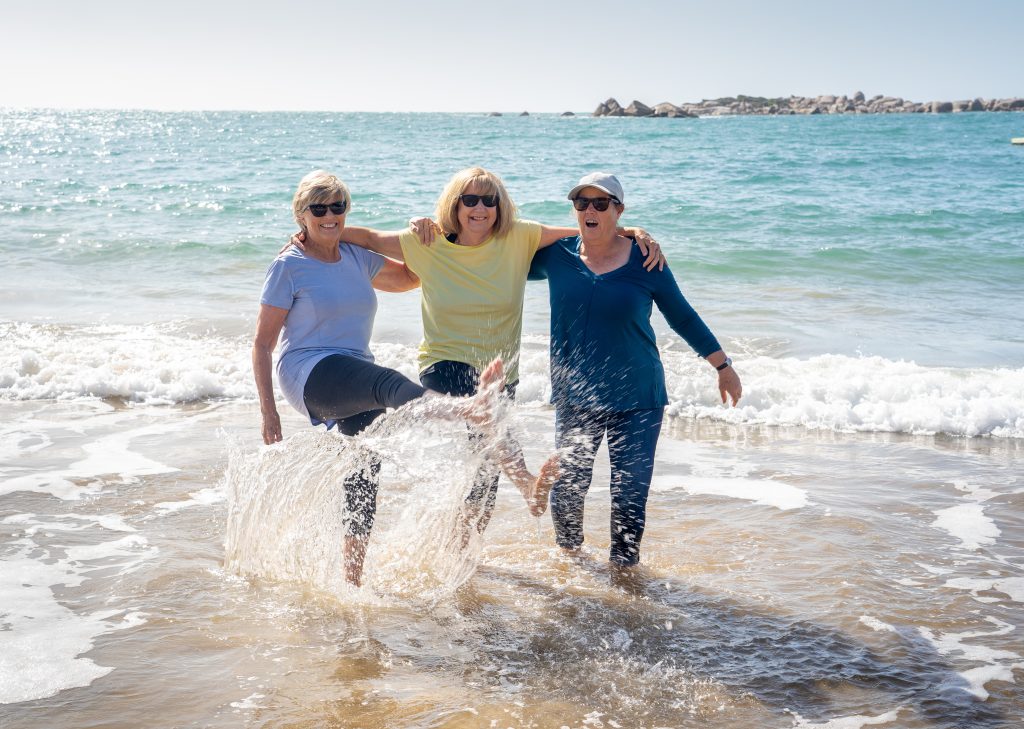 três idosas andando na praia